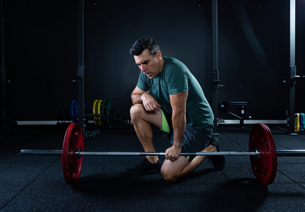 A lifter takes a break by leaning on their barbell. 