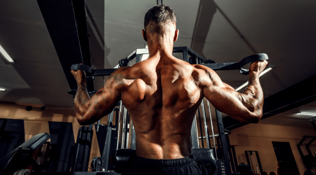 Athlete performs a lat pulldown with his back to the camera. 