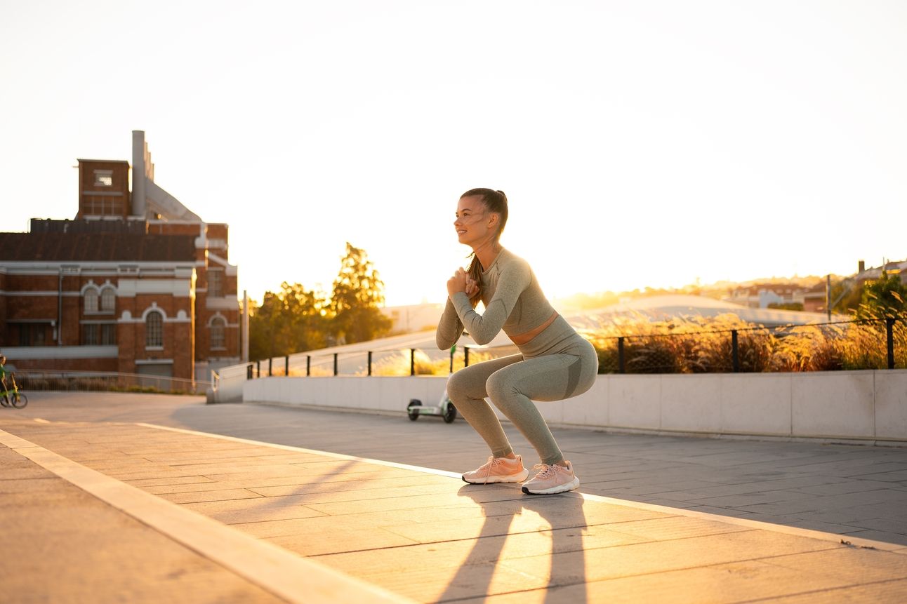 Woman performs body weight squat under a setting sun